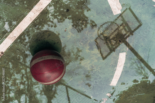 Basketball hoop with reflective water after rain at outdoor basketball court.