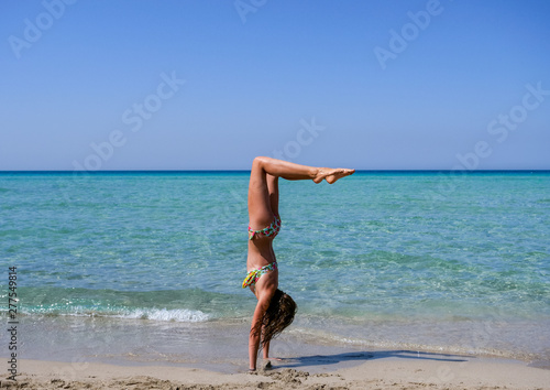 Slim and athletic girl doing yoga, calisthenics, fitness training on a wonderful beach with crystal clear water -vacation-fitness-wellness