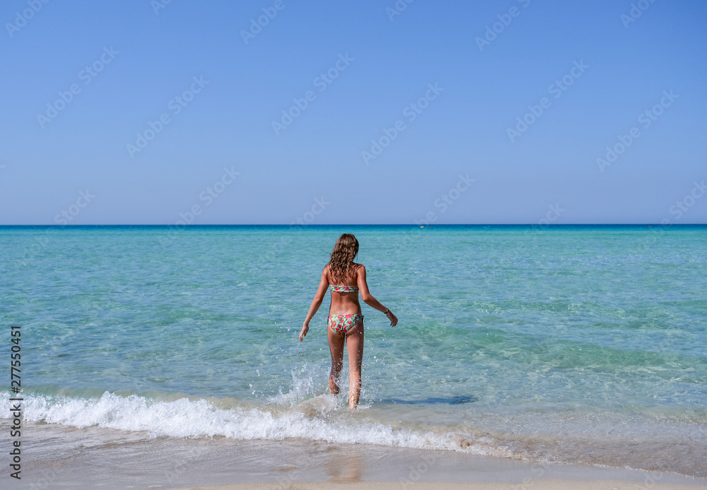Slim and athletic girl in a colourful bikini walking into the crystal clear water of a beautiful beach-vacation-fitness-wellness