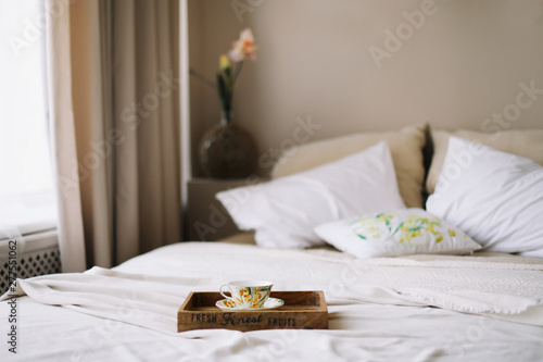 Breakfast in bed. Wooden tray with coffee cup. White bedroom. Good morning