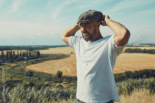 Portrait of confused male farmer looking into the camera and scratching his head. Close up of young doubtful man standing in the meadow on sunny day. Yellow field under blue sky at background.