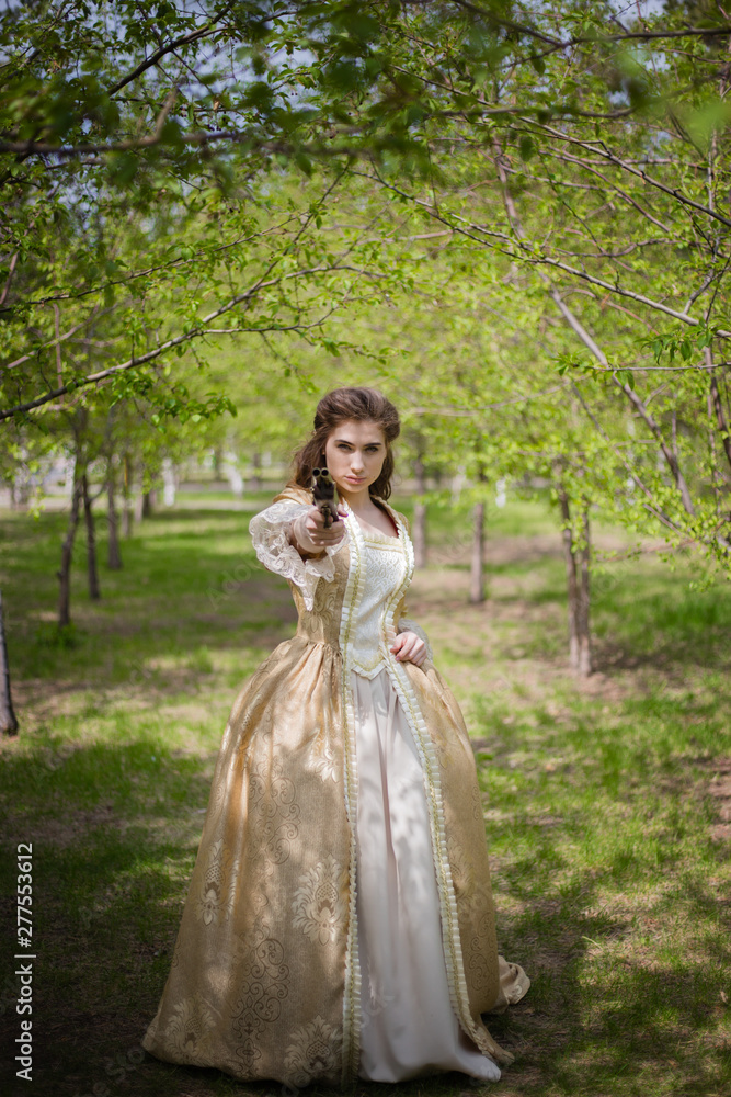 Beautiful girl in a gold dress against a background of green trees. A woman in a ball gown of the Rococo era.