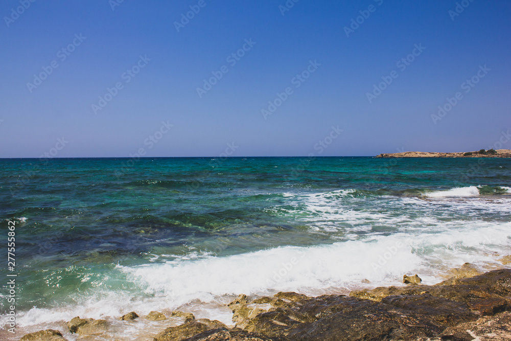 Beautiful view of the clear Mediterranean sea with white foam wave on the rocky shore. Sunny seascape in Cyprus