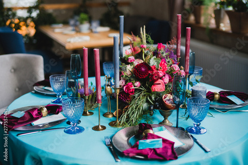 Coziness and style. Modern event design. Table setting at wedding reception. Floral compositions with beautiful flowers and greenery, candles, laying and plates on decorated table.