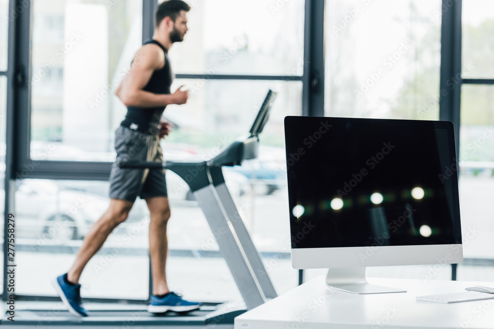 Fototapeta premium selective focus of computer with blank screen near sportsman running on treadmill at sports center
