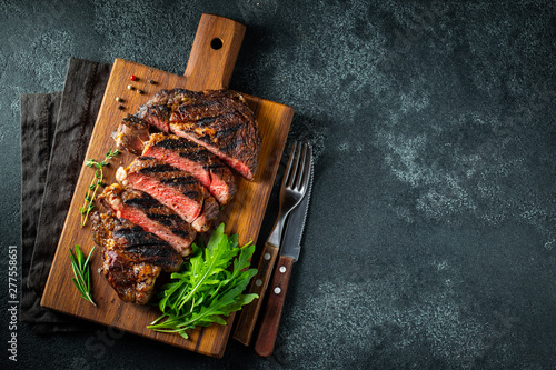 Sliced steak ribeye, grilled with pepper, garlic, salt and thyme served on a wooden cutting Board on a dark stone background. Top view with copy space. Flat lay