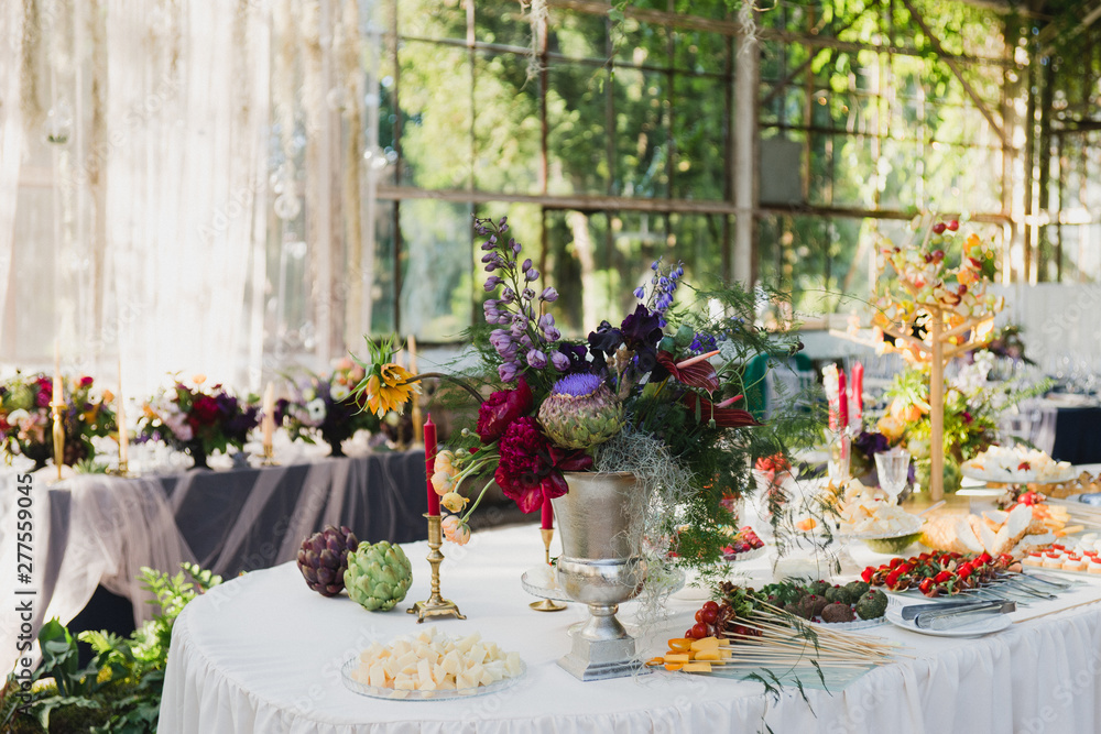 Coziness and style. Modern event design. Table setting at wedding reception. Floral compositions with beautiful flowers and greenery, candles, laying and plates on decorated table. Coziness and style. Modern event design. Table setting at wedding reception. Floral compositions with beautiful flowers and greenery, candles, laying and plates on decorated table.