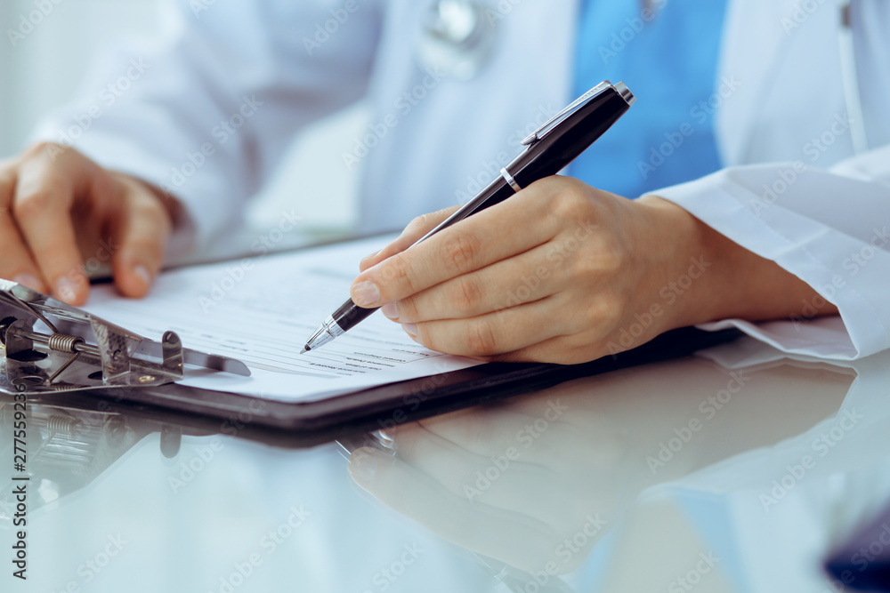 Doctor woman filling up medical form while sitting at the table, close-up of hands Doctor woman filling up medical form while sitting at the table, close-up of hands