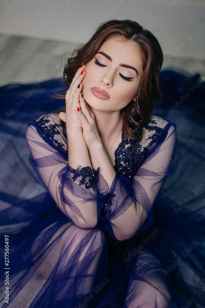 Beautiful girl with big lips. in a blue tulle dress embroidered with beads. Sexy woman portrait. A photo in a white interior. Fashion photo