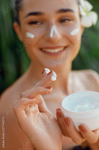 Beauty Woman Concept. Skin care. Young model with Soft skin holding cosmetic cream. Nude make-up. Portrait of female applying moisturizing cream and touch own face. Skin Protection