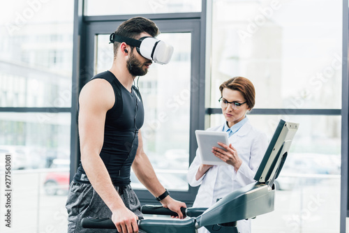 sportsman in vr headset running on treadmill near doctor during endurance test in gym