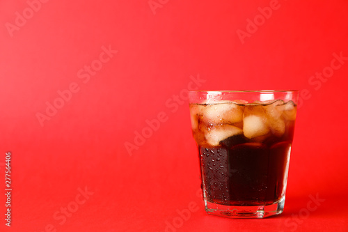 Glass of cold cola on red background, space for text
