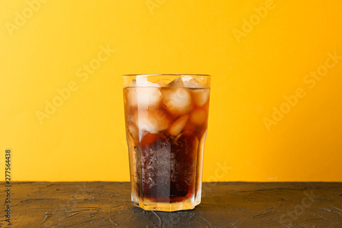Glass of cold cola against color background, space for text