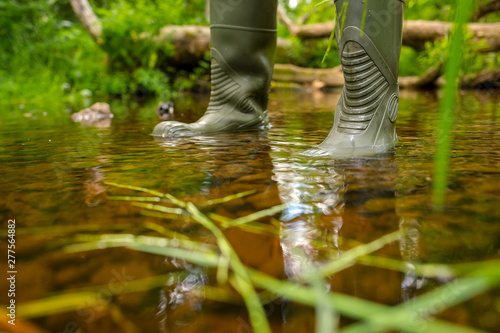 A man in rubber boots is standing in a forest river. Crossing over the creek. Waterproof shoes. Outdoor activities, fishing, hunting and hiking.