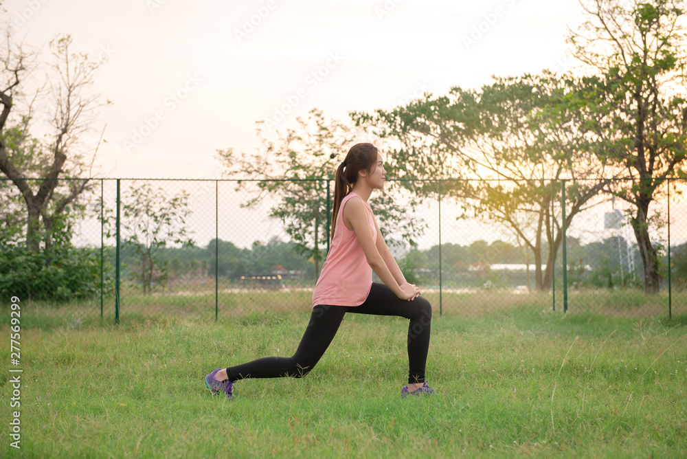 Asian woman sit for stretching body on the lawn in the evening,Thailand people exercise at the park