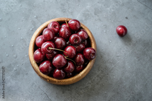 Dark red cherries in a bowl on wooden and gray background 