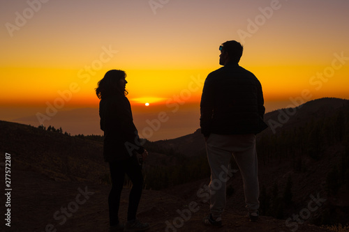 A silhouette of a couple on the top of Teide staring at each other with the sun in the background