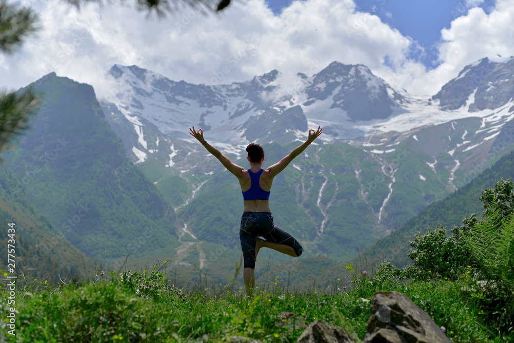 Young sports woman doing yoga on the green grass in the summer on the background of snowy mountains. Young sports woman doing yoga on the green grass in the summer on the background of snowy mountains.
