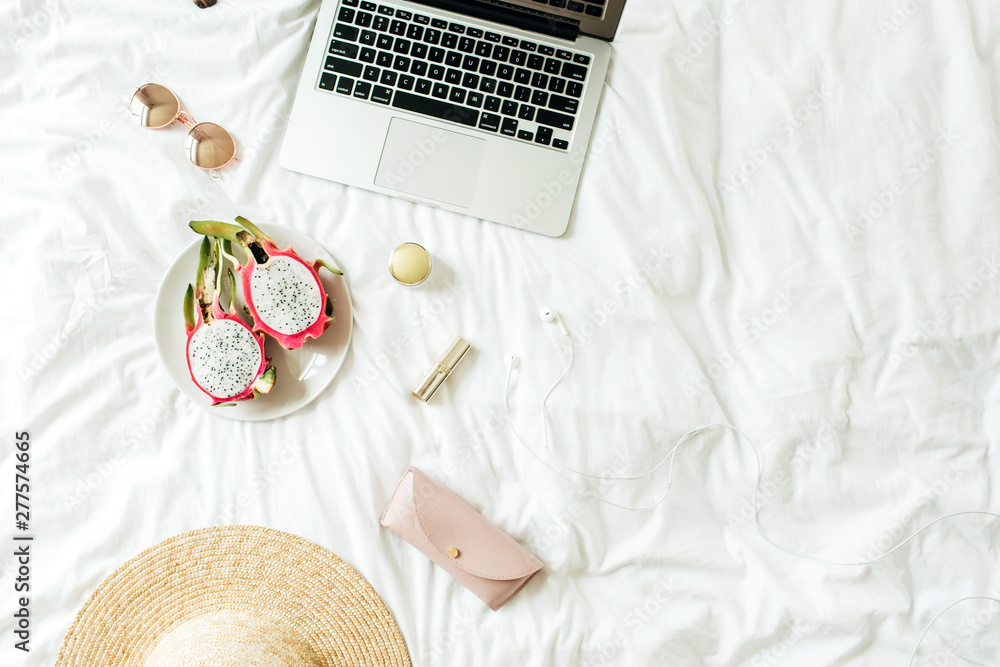 Women's fashion accessories, glasses, lipstick, straw hat, case, headphones  with laptop and exotic dragon fruit lying on bed with white linens. Summer  and travel concept. Top view, flat lay. Photos | Adobe