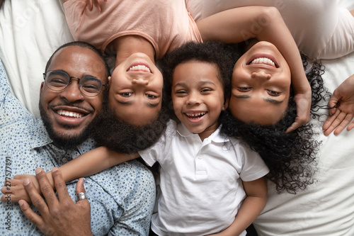 Happy african family lying on bed cuddling, portrait, top view