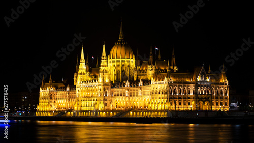 Cityscape of Budapest with bright parliament illuminated and reflection in Danube river. Pink and purple colors of sky reflecting in water during sunset.