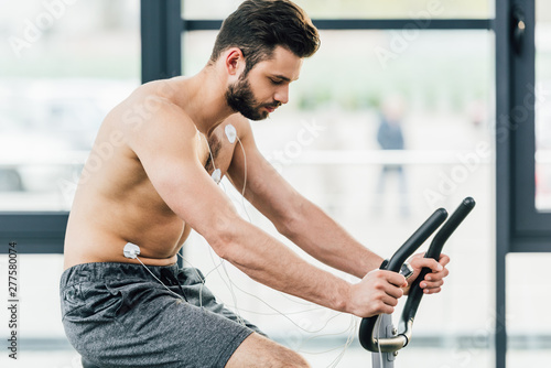 muscular sportsman with electrodes training on elliptical during endurance test in gym