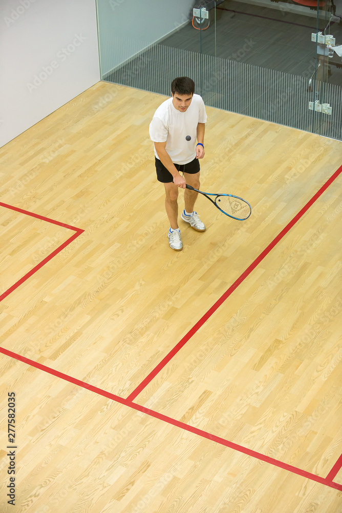 Squash player in action on squash court, front view/Young man playing match of squash Squash player in action on squash court, front view/Young man playing match of squash