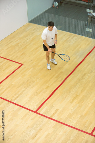 Squash player in action on squash court, front view/Young man playing match of squash
