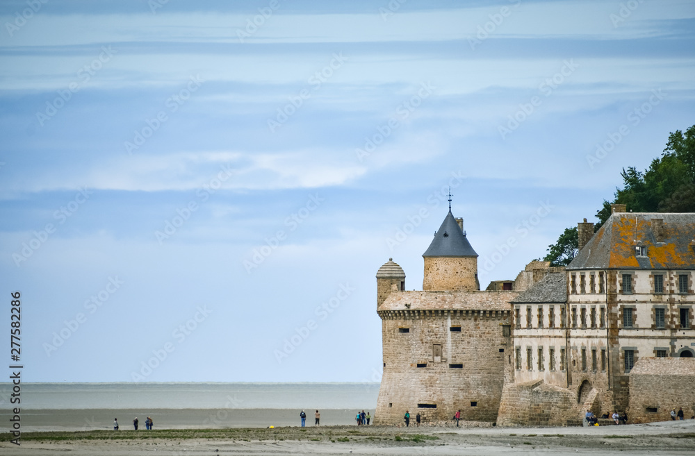 Tourists on the beach and one of the towers of the wall of Mont Saint Michel, France.