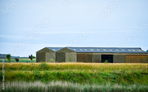 Barn or warehouse between meadows, and farmland. Blue sky for text.
