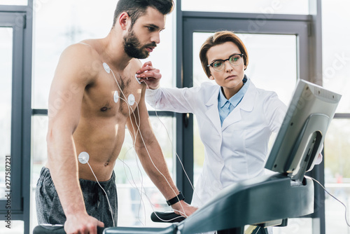 beautiful doctor putting electrodes on shirtless sportsman during endurance test photo