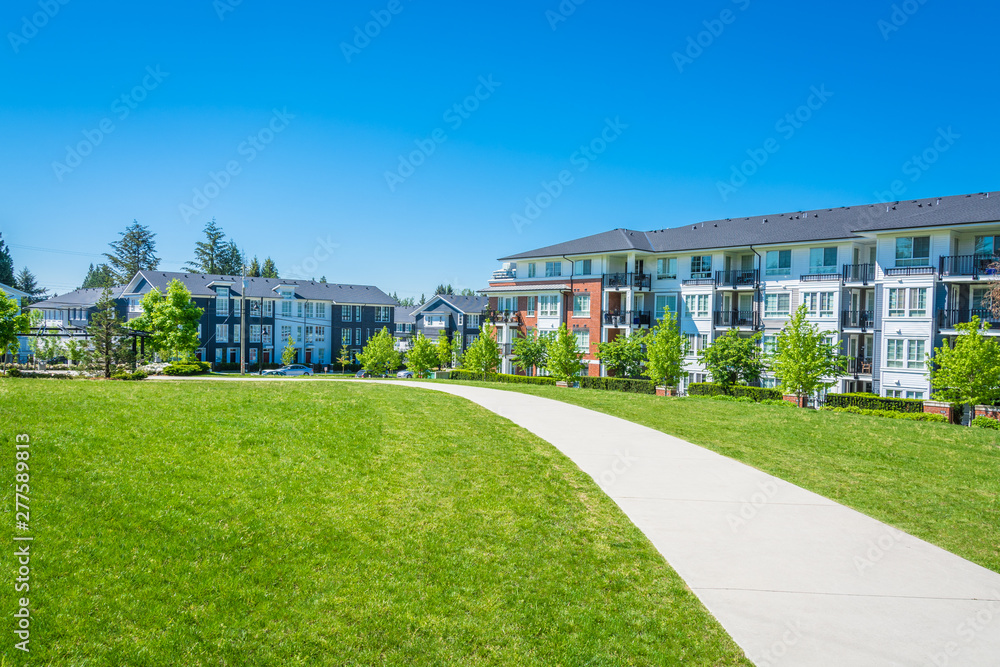 Obraz premium Concrete pathway across huge green lawn in front of residential condo building. Apartment building on sunny day with blue sky.