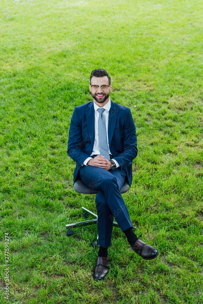 high angle view of happy young businessman sitting in office chair in park and loooking at camera high angle view of happy young businessman sitting in office chair in park and loooking at camera