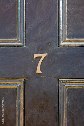 House number seven with the 7 in bronze on a black wooden front door with gold edged carved panels photo