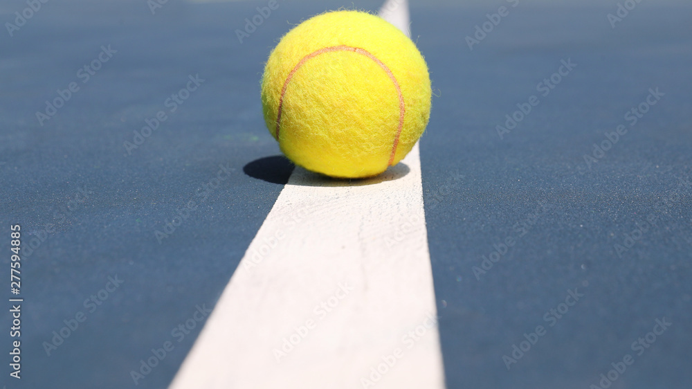 Yellow tennis ball lies on the white line of the court. Close up