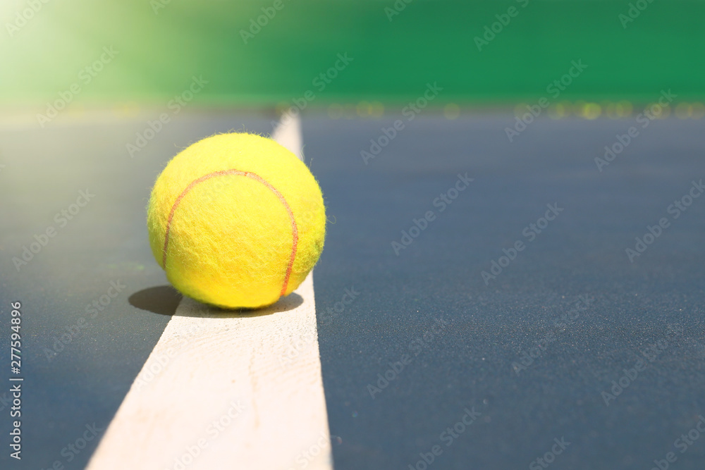 Yellow tennis ball lies on the white line of the court. Close up