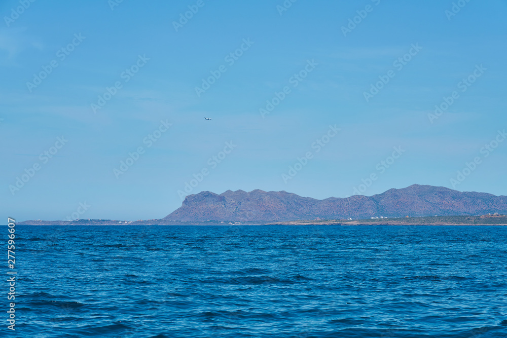 Blue sea water with foggy rocky island on a background under a clear blue sky. Copy space. 