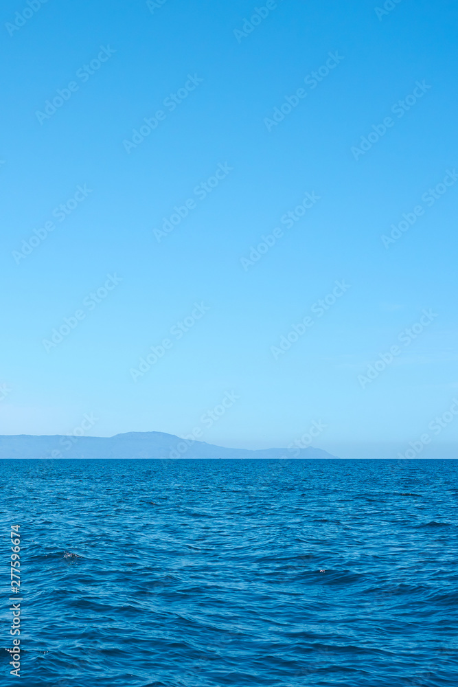Blue sea water with foggy rocky island on a background under a clear blue sky. Copy space. 