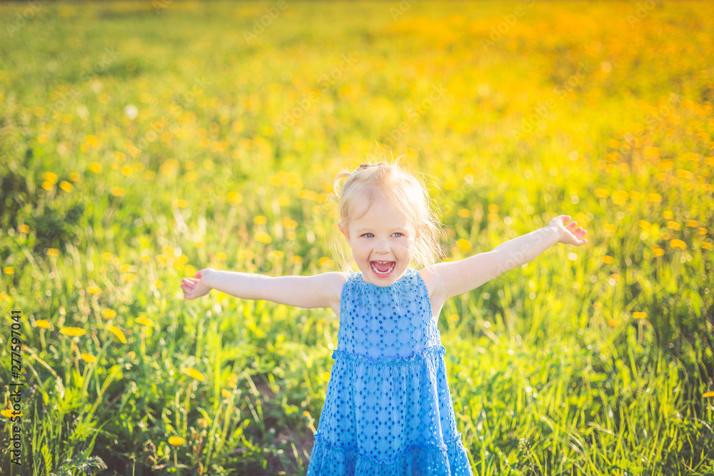 A little girl in a blue dress screams happily, arms outstretched in the middle of a flower field in the summer. A little girl in a blue dress screams happily, arms outstretched in the middle of a flower field in the summer.