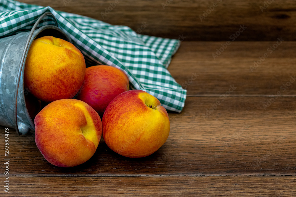 Peaches in a bucket with green picnic tabletop over wooden background with copy space Peaches in a bucket with green picnic tabletop over wooden background with copy space
