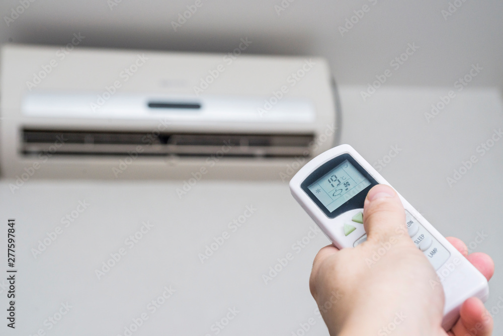 Hand with remote control directed on the conditioner on the wall. Air conditioner with remote controller