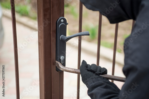 Burglar trying to break the gate with a crowbar. Thief breaking lock to open the gate