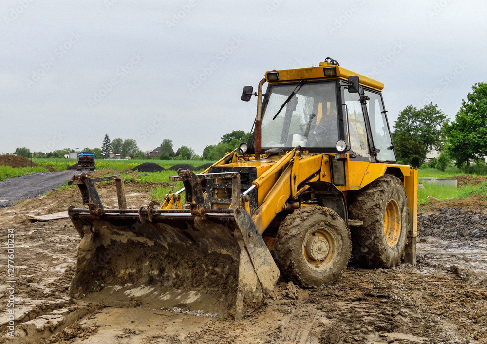 A yellow tractor building a new house in a wet weather A yellow tractor building a new house in a wet weather