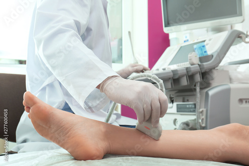 Doctor conducting ultrasound examination of patient's leg in clinic, closeup photo