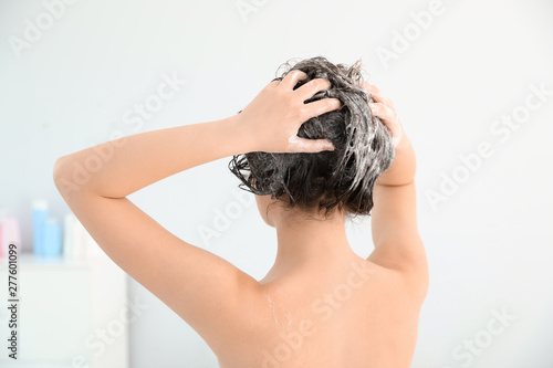 Woman applying shampoo onto her hair in light bathroom