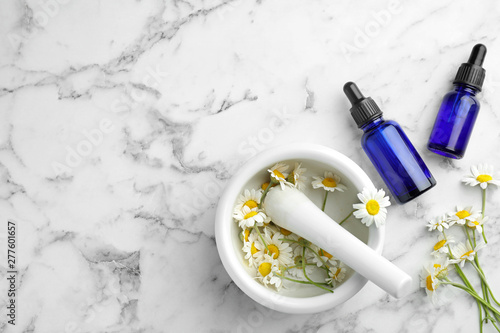 Flat lay composition with bottles of chamomile essential oil and flowers on marble table. Space for text