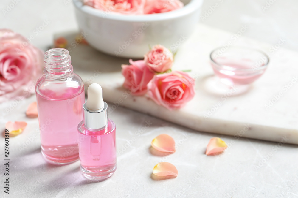Bottles of rose essential oil and fresh flowers on table, space for text Bottles of rose essential oil and fresh flowers on table, space for text