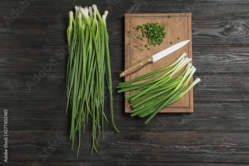 Flat lay composition with green onions, knife and board on dark wooden table