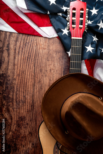 Obraz na płótnie American culture, living on a ranch and country music concept theme with a cowboy hat, USA flag and acoustic guitar on a wooden background in a old saloon with copy space w salonie