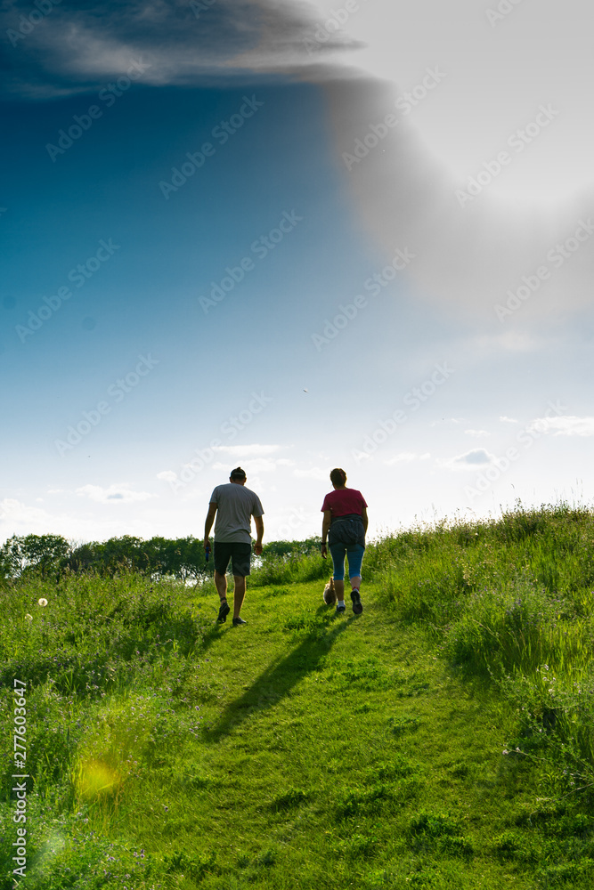 Couple hiking in fields of grass along a lake blue skys and reflections in water